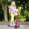 little child learning to ride a scooter in a city park on sunny summer day. cute preschooler girl in safety helmet riding a roller. kids play outdoors. active leisure and outdoor sport for children.